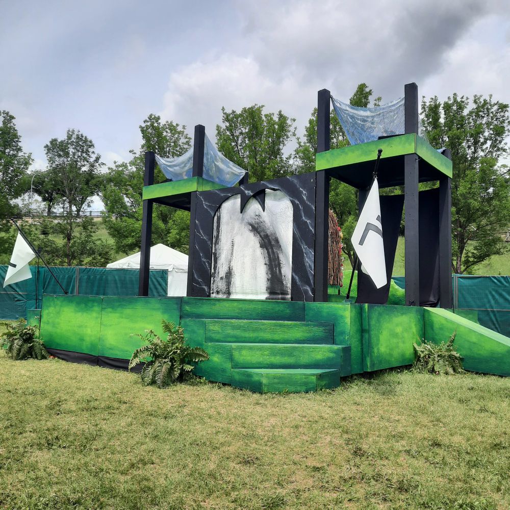 Outdoor stage with black arch and green stairs on set. 