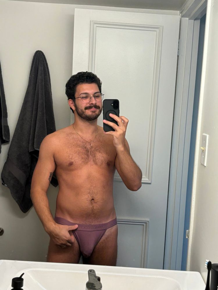 Photo of me shirtless in a purple jockstrap from the front wearing glasses and smiling 