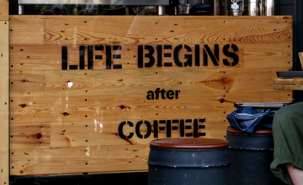 Eun Holzschild mir der Aufschrift "Life begins after Coffee" an einem Cafe. 