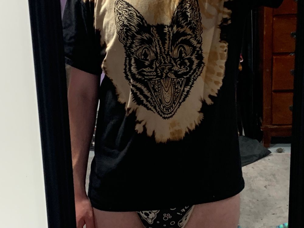 A cool punk tshirt of a scary looking cat design, with a thick diaper underneath a onesie poking out