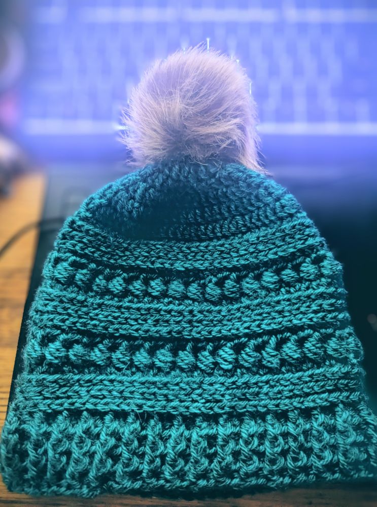 A crocheted toque in emerald green with a brown faux fur pom-pom.