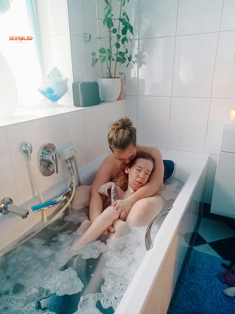 Alex und ich sitzen in der Badewanne. Mein Rücken ist an ihren Oberkörper gelehnt. Mein Kopf lehnt sich an ihren linken Oberarm, während ihr rechter Arm meine Beine unter den Knien hält und mich an sie drückt. Ihr Kopf ist gesenkt, weil sie mich auf den Hinterkopf küsst.

Das Bad ist weiß blau gefließt. Durch ein Fenster fällt Licht. Links hinter uns stehen Pflanzen und ein paar Bücher.