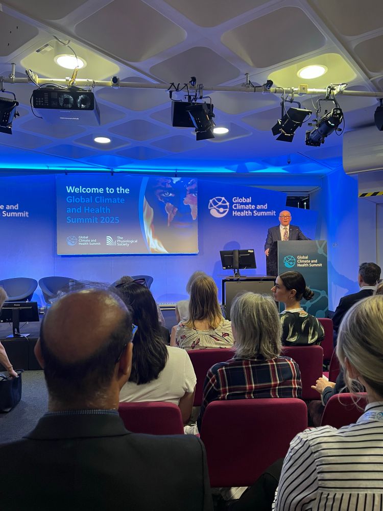 Prof Mike Tipton introducing the conference, standing at a podium in front of a presentation slide with the words welcome to the global climate and health summit 2025