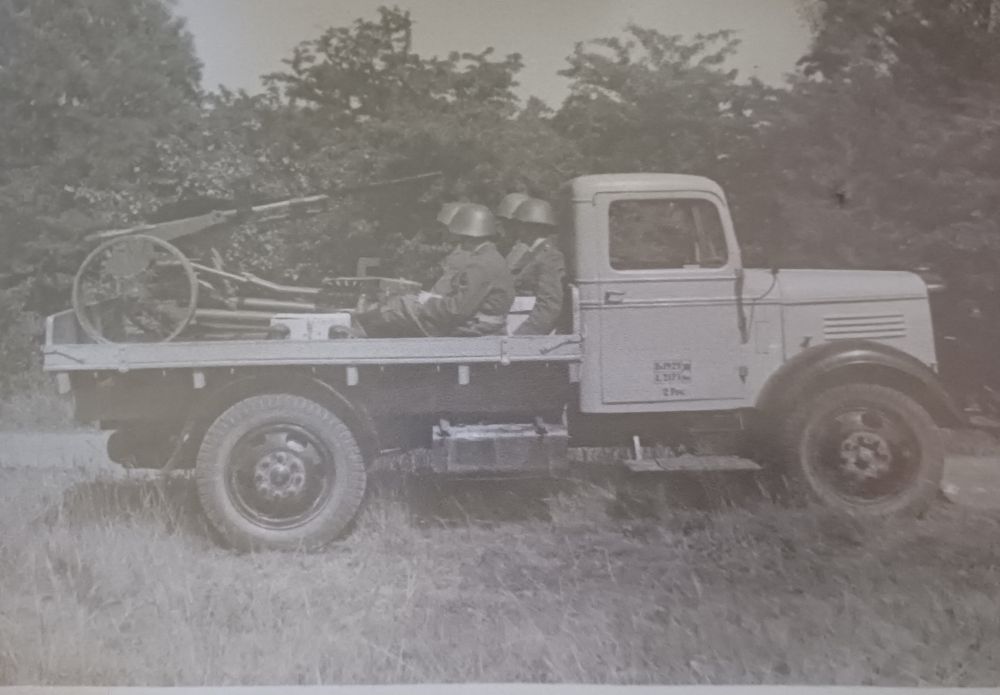 Two soldiers and a cannon sitting in the back of a lorry.