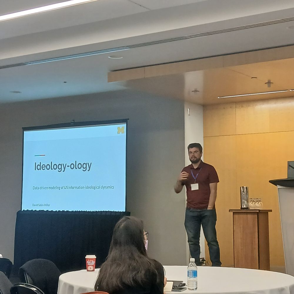 Photo of David introducing the talk with a slide titled Ideology-ology.