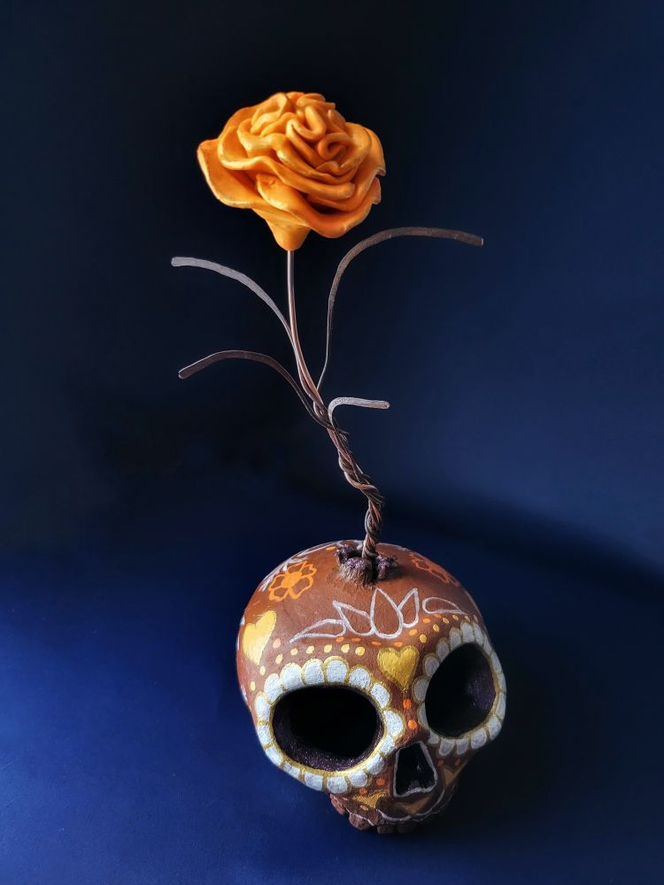 Mixed media sculpture of a painted skull with a flower growing out from the crown 