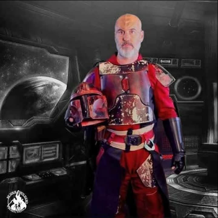 A man dressed in a red-hued Mandalorian costume from the Star Wars universe, with ridges on his head to mimick a Klingon from Star Trek