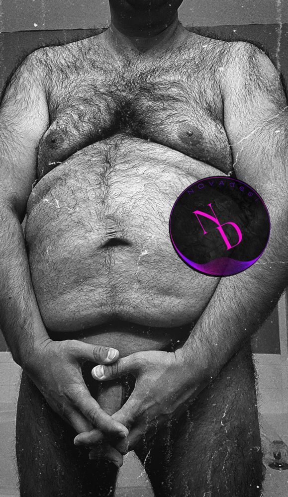 NOVAdesi, a chubby, hairy, faceless Indian sex worker is standing up naked. He has a fat belly, big moobs, thick thighs, and lots of body hair, especially in the chest area. He has his hand covering up his uncut cock and balls, though we see a bit of his veiny shaft. The pic is in the form of a nude, black and white, monochromatic selfie and the subject identifies as a daddy dom top bear, bull, swinger, nudist, exhibitionist, and nsfw body positive OnlyFans content creator based in the DMV for all the gay boys, horny girls, and chubby chasers. 🧡🖤