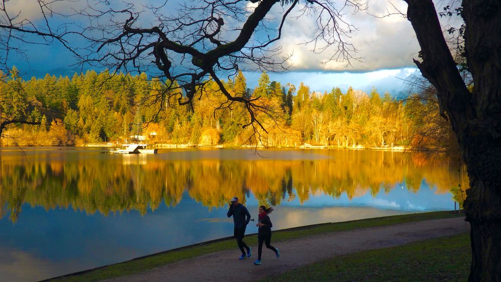 Two joggers passing sunlit Lost Lagoon in Vancouver