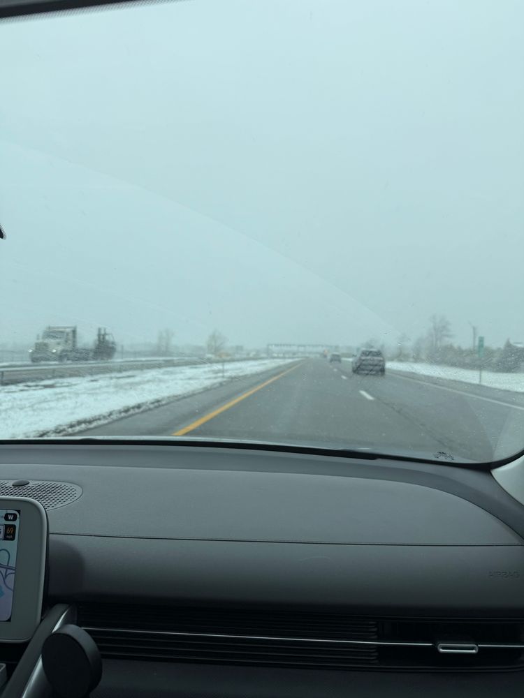 A picture of a highway from a car with snow on the sides of the road. 