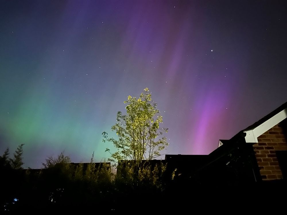Pink, purple and green aurora and stars over houses in Sussex, UK