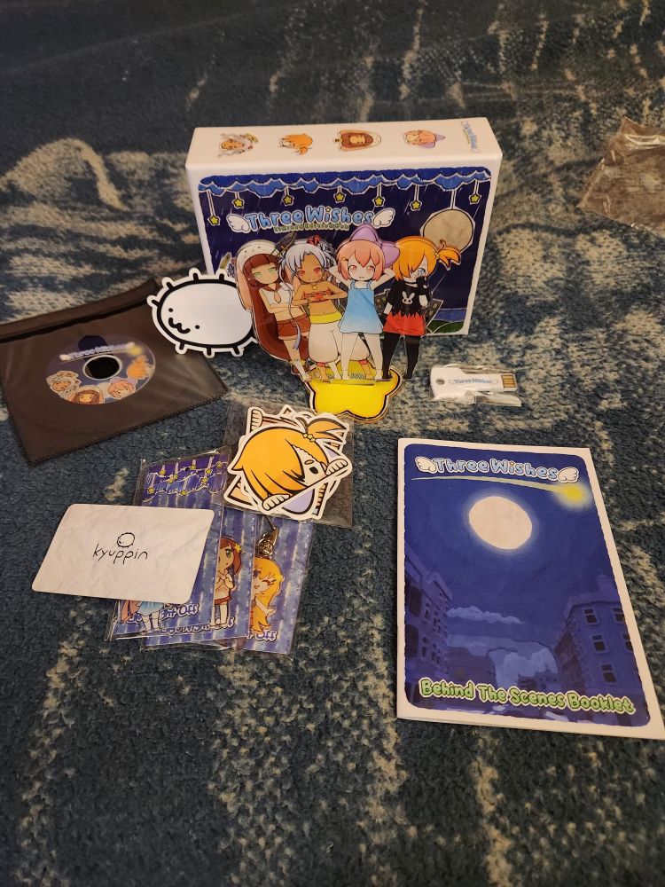 The spread of goodies inside the box which includes the game on a key shaped USB drive, an acrylic standee of the characters together, an onionbug sticker, CD soundtrack, Three Wishes stickers, a making of booklet, and a little card with Kyuppin's logo and an onionbug.