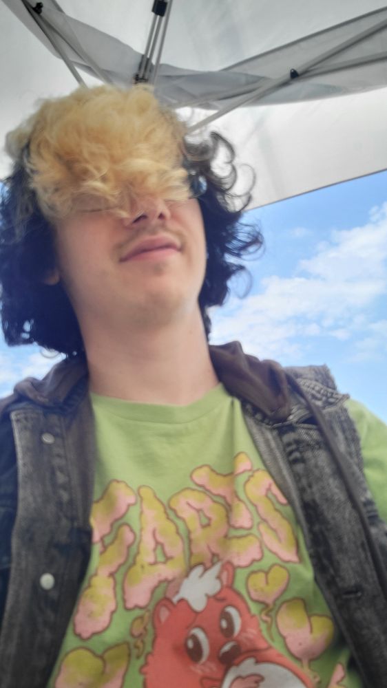 Look at this mf fool with a green Farts Are My Language (with a farting skunk) shirt on, rocking black and blonde striped skunk style hair.