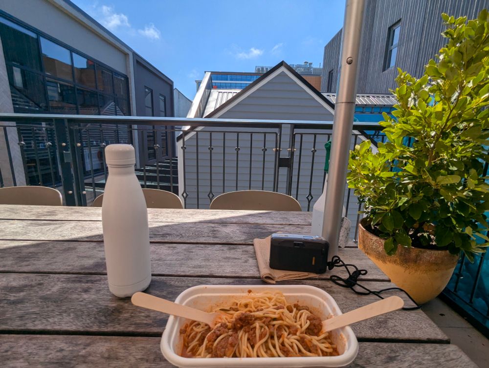 A view from the outdoor seating at the Riverside market, showing my meal (Spaghetti Bolognaise) as well as the second floors and rooftops of buildings surrounding me