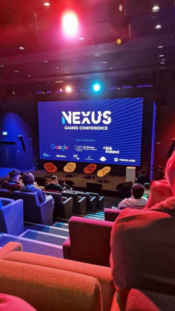 Photo of the Nexus stage. The projector reads "Nexus game conference" and has a list of partners below it. 