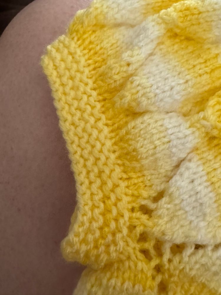 Close up of a knitted garter stitch sleeve on a baby sweater with a diamond-shaped lace pattern in shades of yellow and white. 