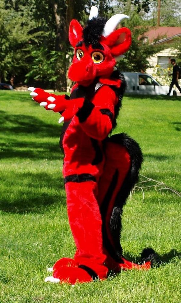 A red dragon fursuit with black stripes poses in a field 