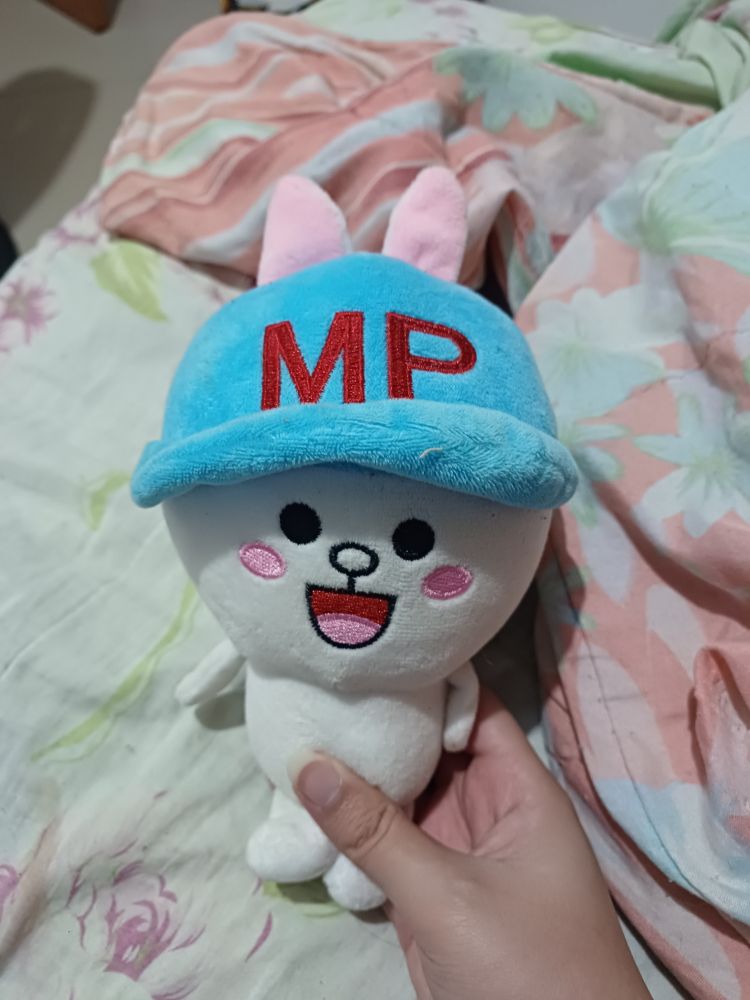 uma pelúcia de coelhinho branco cabeçudo com um boné azul. nele, as letras "MP" em vermelho 