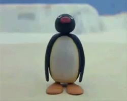 a penguin with a red beak is standing on a sandy surface .