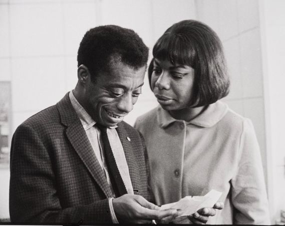 The image captures a close, personal moment between American author and activist James Baldwin and American singer, songwriter, and civil rights activist Nina Simone. 

The photograph, taken by Bernard Gotfryd in 1964. It shows Baldwin and Simone looking at a document in Baldwin's hands while engaged in conversation. Ms. Simone, on the right, is dressed in a white, button-down round-collared, blouse; Baldwin in a dark sport jacket, white shirt and thin, black necktie.