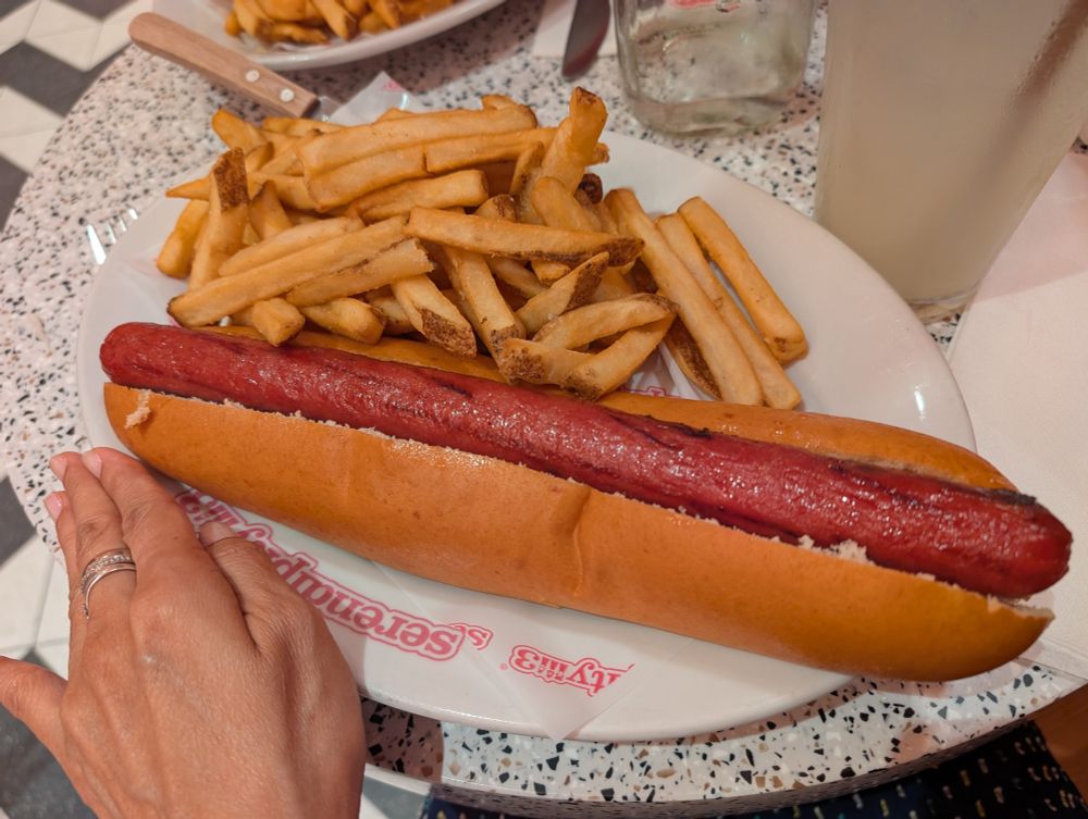 My hand next to my lunch plate of a foot long hot dog and fries at Serendipity3.