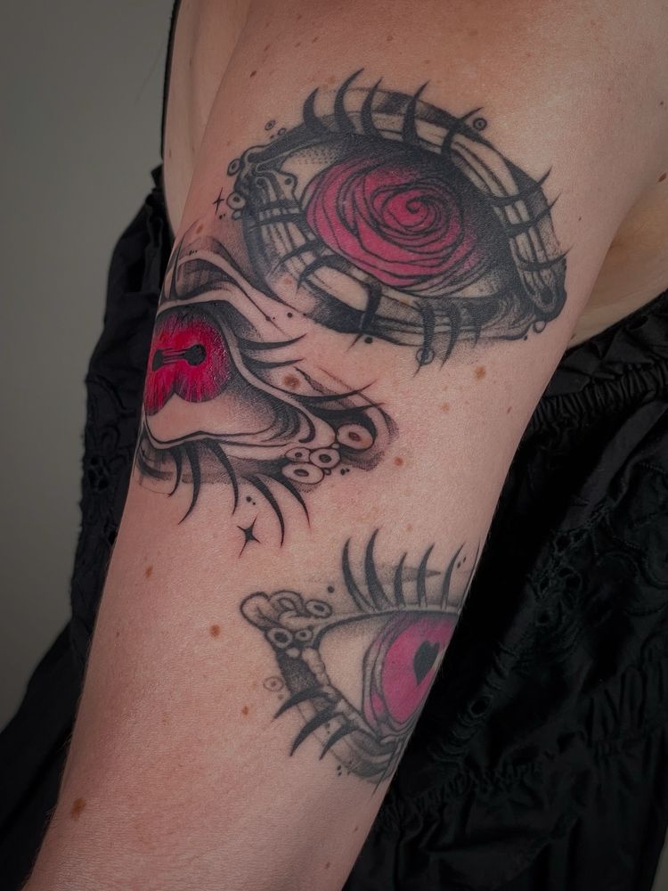 Sentinel eye blackwork tattoo with pink iris on upper arm