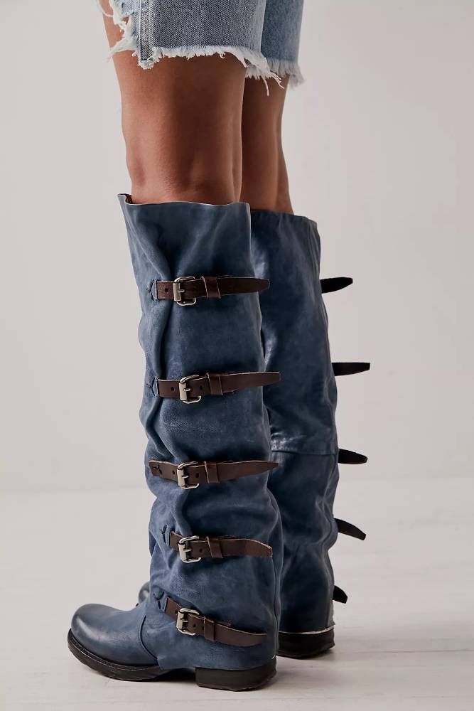 From the knees down: a model wearing denim boots with 5 horizontal buckled belts (ostensibly holding them on, but unclear whether they're functional or purely decorative).