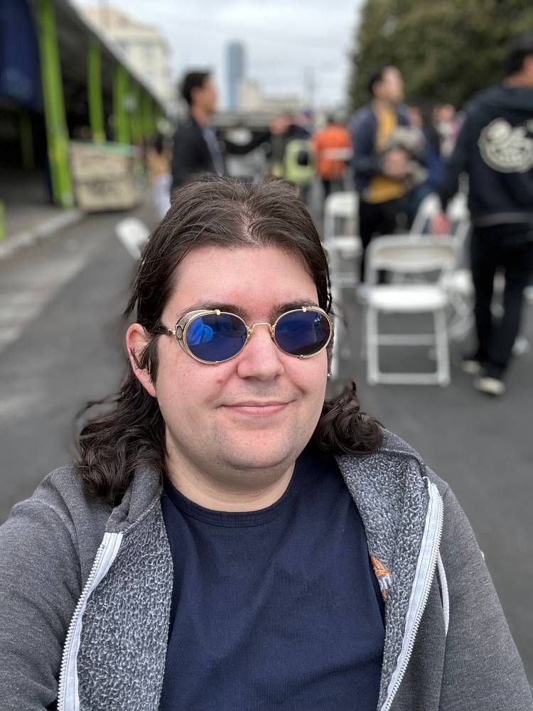 Outdoor selfie wearing gold sunglasses with metal mesh side shields and dark blue mirrored transitions lenses, which have darkened in the sun.