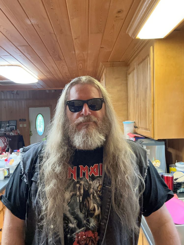 Male with long hair, beard, and sunglasses wearing a denim vest over an Iron Maiden shirt