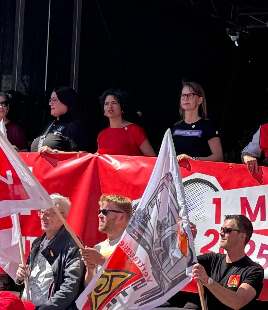 Ina Morgenroth, Tanja Chawla und Sandra Goldschmidt hinter dem DGB-Banner zum 1. Ai, davor Ole Borgard und Olaf Harms mit ver.di Fahnen sowie ein Kollege mit einer IG Metall Fahne. 