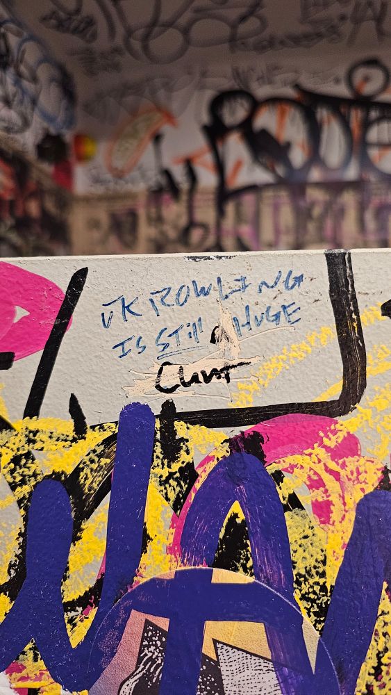 Graffiti on a stall wall that reads, "JK Rowling is still a huge cunt" surrounded by other graffiti