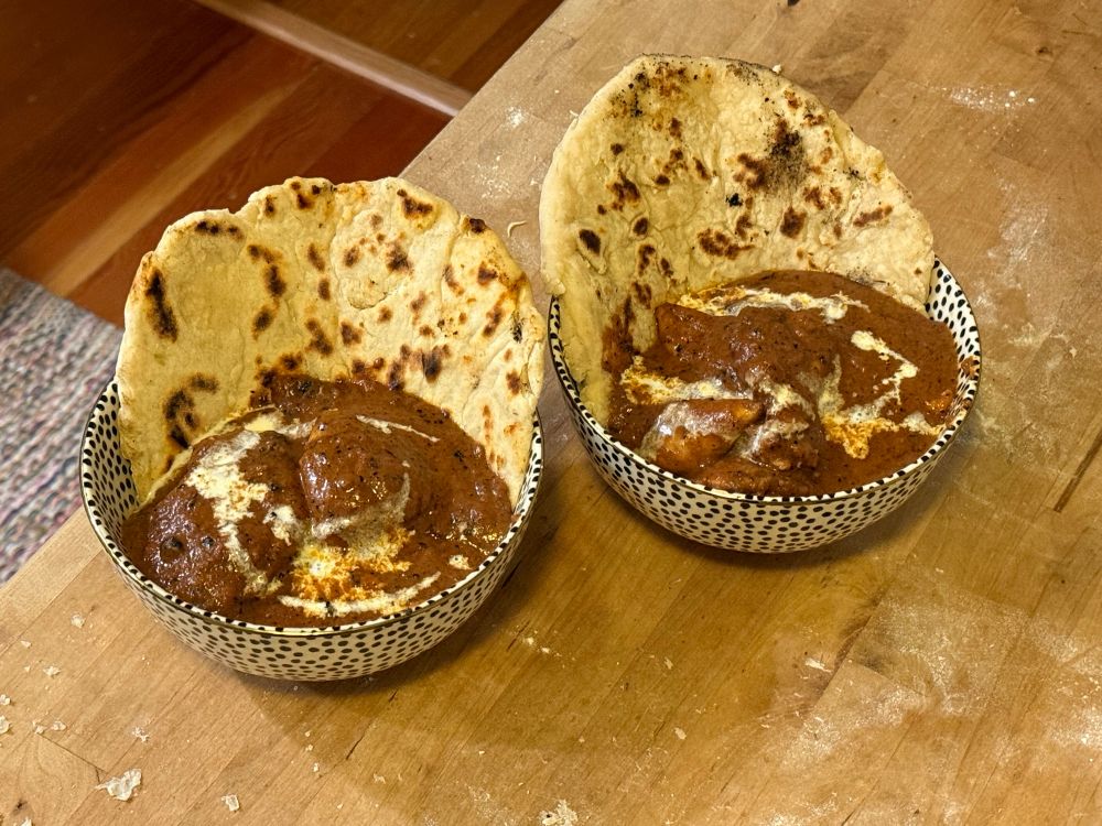 Two steaming bowls of delicious butter chicken each with a slice of homemade naan dipped into them