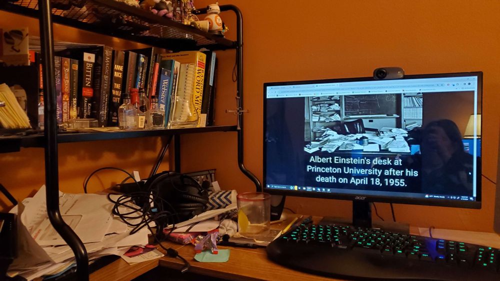 A messy desk with a monitor showing Albert Einstein's messy desk.