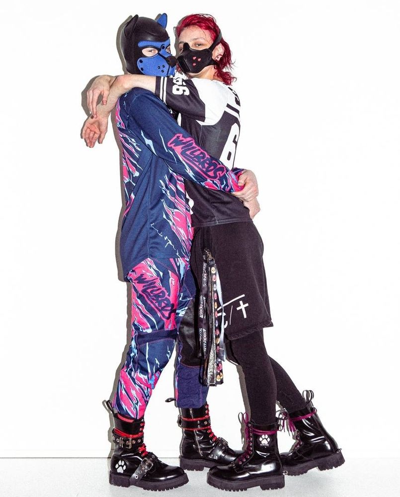 Fyre in blue hood. Blue and pink MX gear and Red Booties.

Sinner in half face hood with spikes, long red hair. Wearing shorts, a black and white jersey. Lanyards hanging from her pocket. Purple Booties.