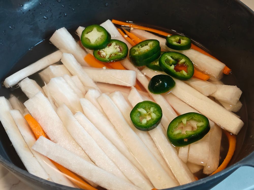 sliced sticks of daikon and carrot and round slices of jalapeño are brining in a bowl