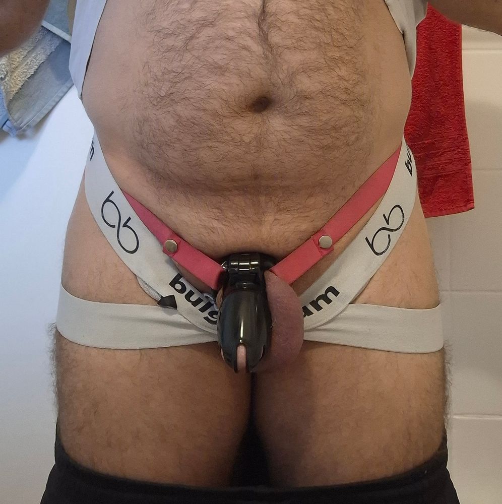 Man in white jockstrap and a plastic chastity cage, showing off his belly.