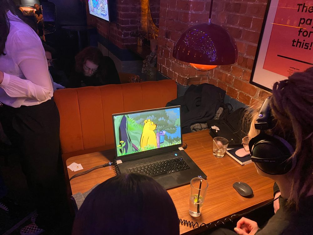 a laptop on a table is running Winnie’s Hole; folks are playing and watching 