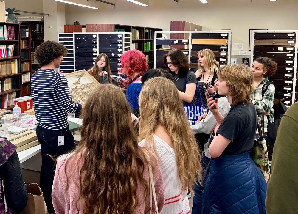 A group of high school students surrounding a museum curator holding a box of moths 