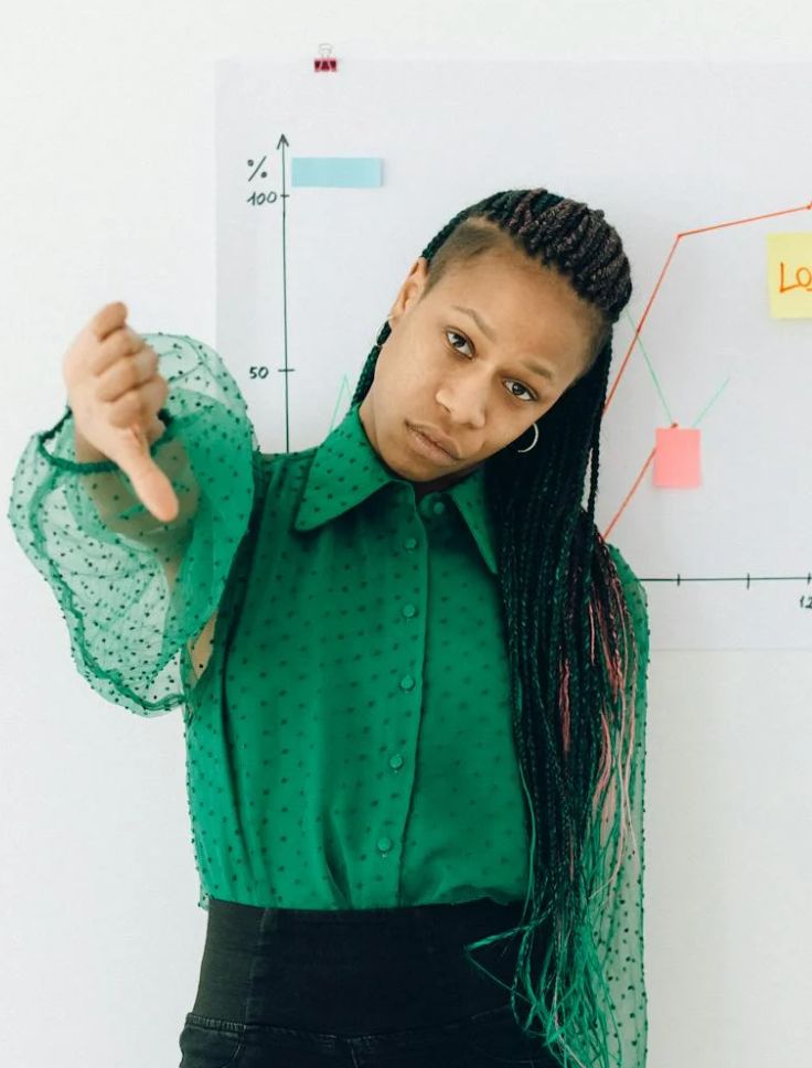Woman standing in front of a white board with a diagram giving the thumbs down with a "tired of this" look on her face.
