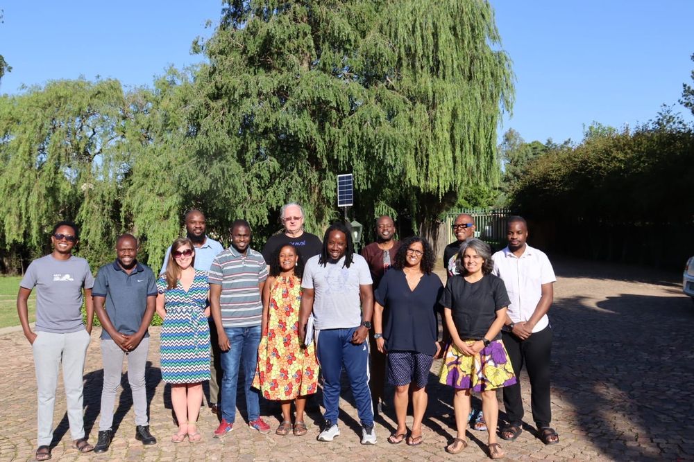 Group of 13 people standing in front of lush green trees