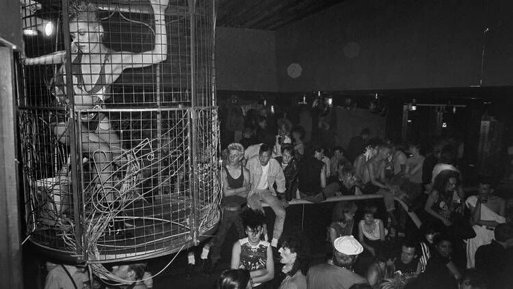 Batcave night photo depicting a dancing woman in a cage and various spookies milling about the environs.