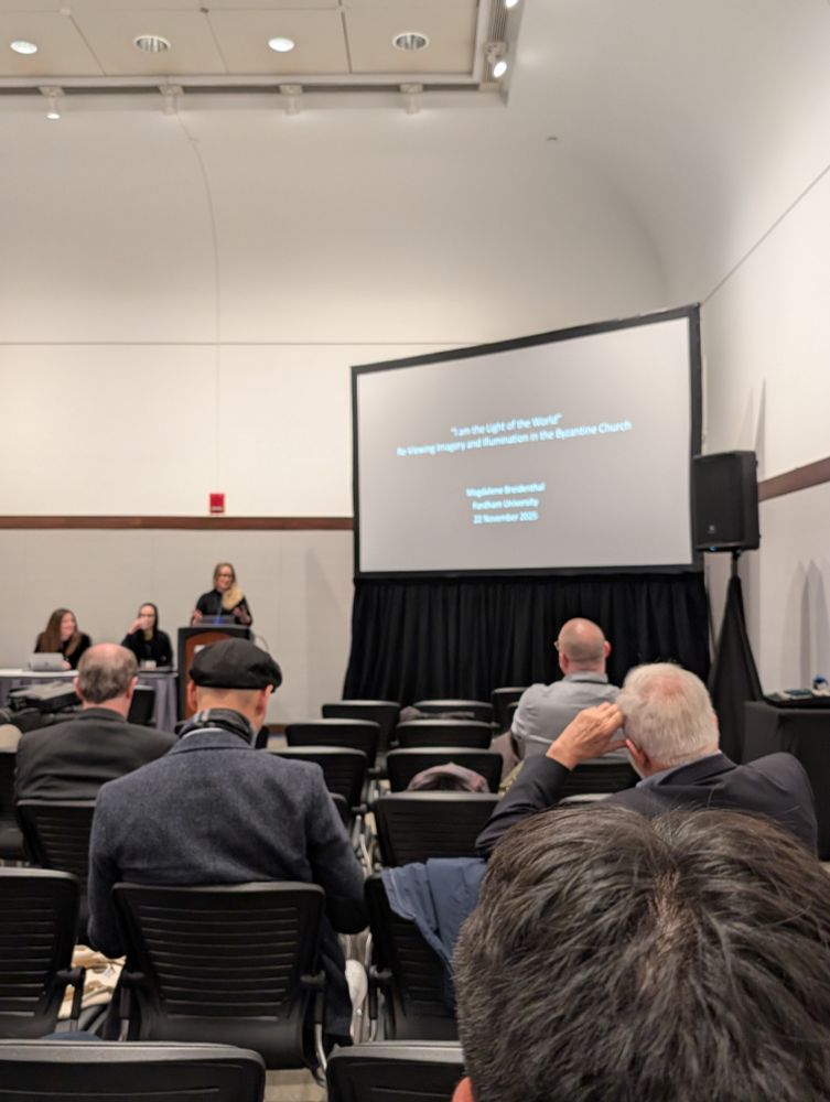 Picture of a seminare room. Magdalene Breidenthal standing at the lectern, 1st PowerPoint slide shown on the screen next to her. 