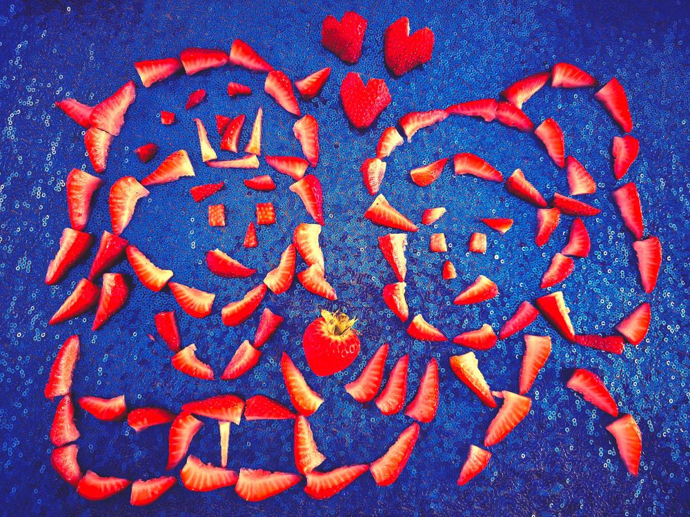 An arrangement of sliced strawberries made to look like Johnny Joestar lovingly handing Rina Higashikata a strawberry. There are strawberries cut into hearts floating above them as they both smile at one another.