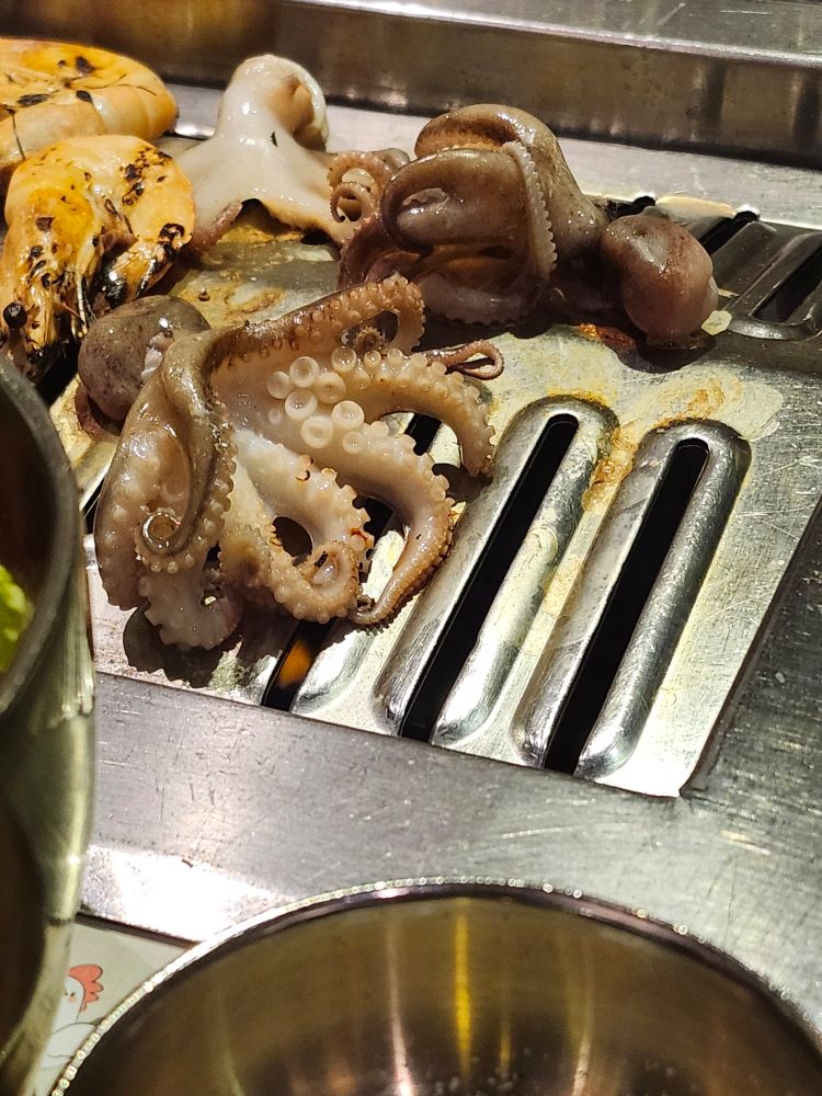 A photo of overcooked shrimp on the top left corner, mackerel skin, and two baby octopus on grill.