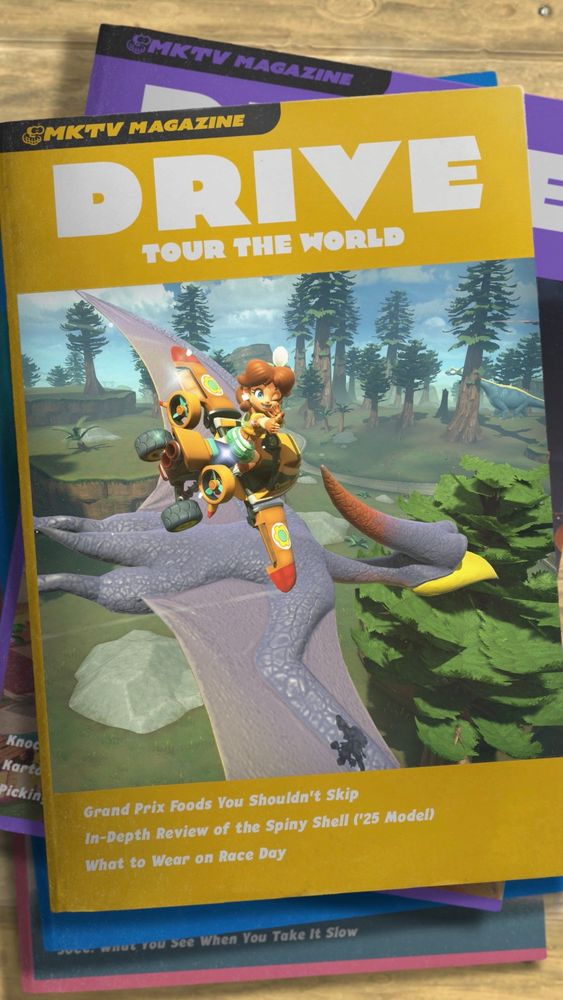 A screenshot from Mario Kart World. It shows a stack of magazines titled «MKTV Magazine», with the words «Drive - Tour the world» above a picture of Daisy flying above a giant pterodactyl in the jungle. A sauropod is barely visible in the background.
