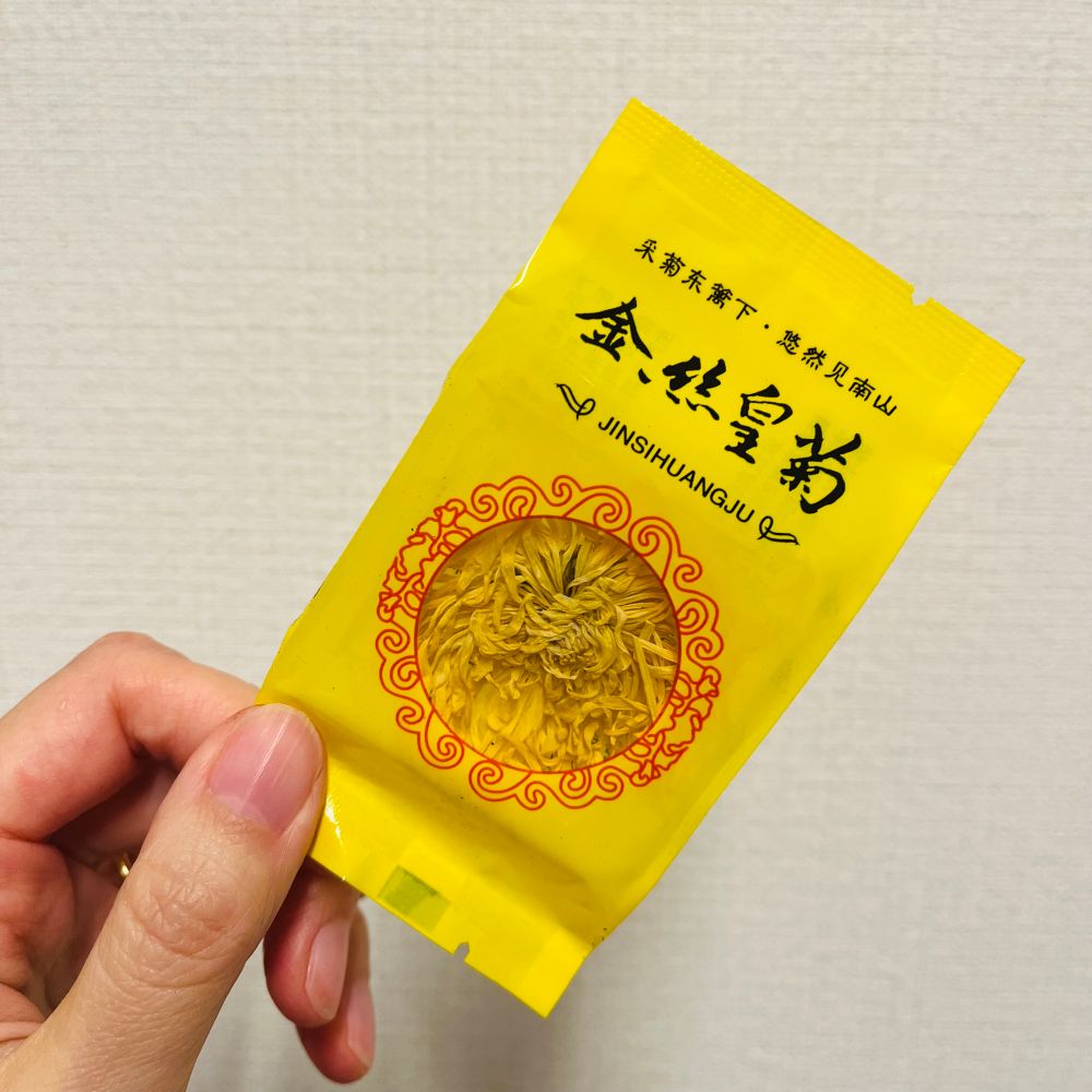 パックされたお茶用の菊の花の写真 黄色いパッケージに金絲皇菊と書かれており、その下の赤い模様で縁取りされた丸い窓から菊の花が見える