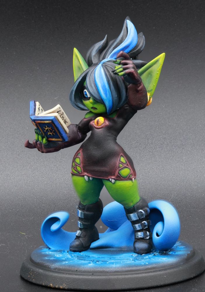Goblin woman, wearing a mini dress that is also a mimic stands on a magic circle, magic tome in one hand, other raised above her head. 