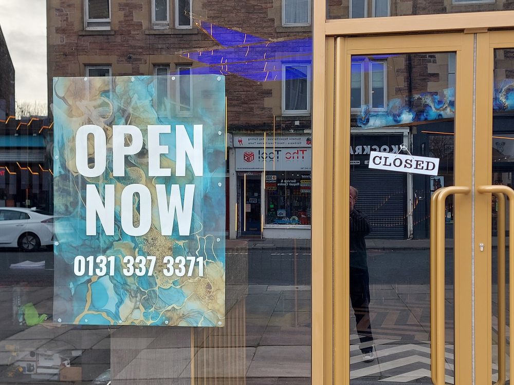 'Open now' sign on a window. 'Closed' sign on the door next to it.