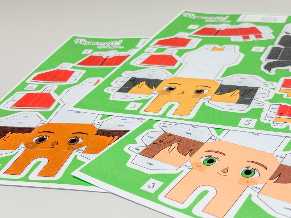cartelas de papel para montar bonecos. a imagem mostra três cartelas coloridas com figuras de bonecos, cada uma com um rosto grande, olhos expressivos e cabelos de diferentes cores. o fundo das cartelas é verde. ao redor dos rostos há várias peças destacáveis, como braços, pernas e roupas vermelhas, todas numeradas para montagem. esses recortes serão dobrados e encaixados para criar um boneco em 3D de papel.