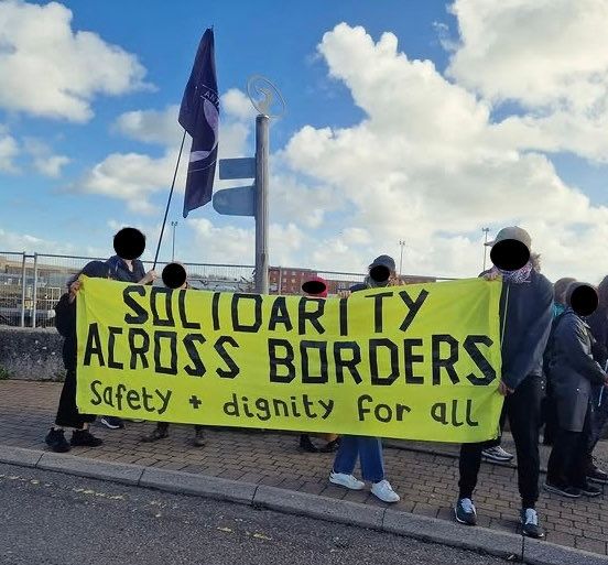 Brighton antifascists holding a banner that reads: solidarity across borders, safety and dignity for all.